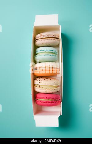 Macarons colorés. Petits gâteaux français. Macarons français doux et colorés dans une boîte sur fond bleu. Cadeau pour la Saint-Valentin Banque D'Images