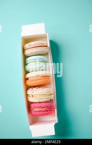 Macarons colorés. Petits gâteaux français. Macarons français doux et colorés dans une boîte sur fond bleu. Cadeau pour la Saint-Valentin Banque D'Images