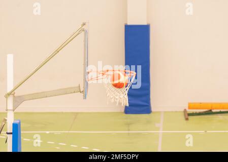 vue latérale d'un basket-ball entrant dans un mini-panier de basket-ball sur un terrain sans parquet, couleur verte Banque D'Images