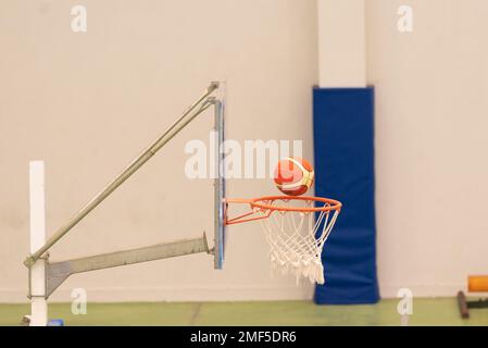 vue latérale d'un basket-ball entrant dans un mini-panier de basket-ball sur un terrain sans parquet, couleur verte Banque D'Images