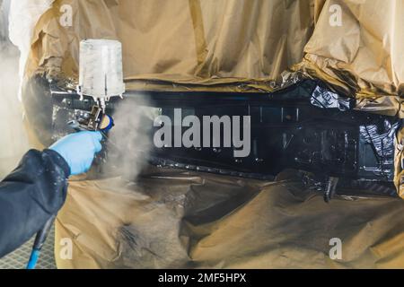 Personne méconnaissable en uniforme de travail portant des gants peignant une partie découverte de la voiture à l'aide d'un aérographe. Peinture automobile. Tir en retrait horizontal. Photo de haute qualité Banque D'Images