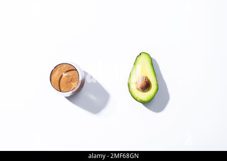 Verre avec smoothie au chocolat à l'avocat et moitié de fruit à l'avocat sur fond blanc au soleil. Vue de dessus, plan d'agencement. Banque D'Images