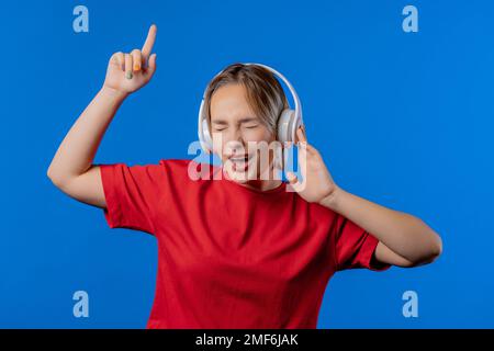 Joyeux adolescent écoutant de la musique, en appréciant la danse avec des écouteurs sur le bleu Banque D'Images