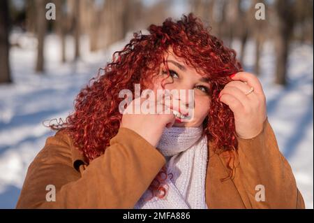 Portrait d'une femme souriante aux cheveux rouges lors d'une promenade en hiver. Banque D'Images