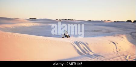 Désert, moto et sports extrêmes d'un homme sur des dunes de sable en Afrique faisant du sport fitness. Défi de conduite, aventure à la plage et voyage à vélo d'un Banque D'Images