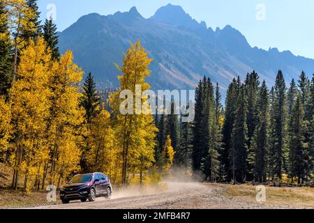 SUV sur Autumn Mountain Road - Un SUV qui déchaîne une route sinueuse dans une vallée colorée au pied de la chaîne des Sneffels par une belle journée d'automne. Banque D'Images