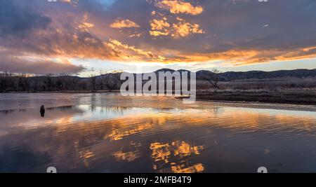 Burning Sky - des nuages colorés au coucher du soleil planant sur une baie à moitié gelée du réservoir de Chatfield lors d'une soirée d'hiver calme. Parc régional de Chatfield, Colorado, États-Unis. Banque D'Images