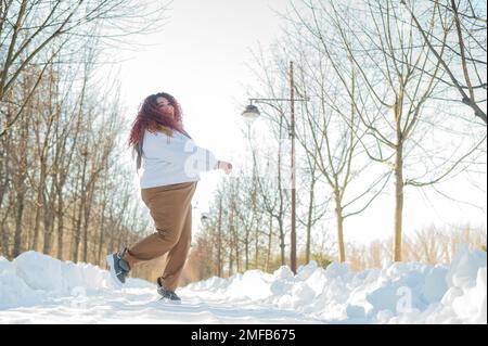 Femme souriante à tête rouge en train de courir au parc en hiver. Banque D'Images