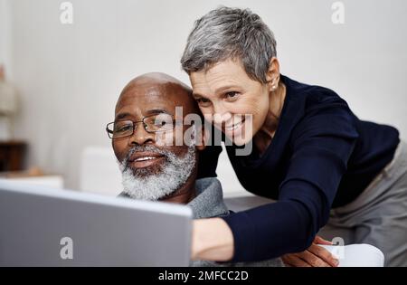 Shes m'enseigne toujours de nouvelles astuces sur l'ordinateur portable. un couple senior affectueux utilisant un ordinateur portable ensemble tout en se relaxant sur le canapé à la maison. Banque D'Images