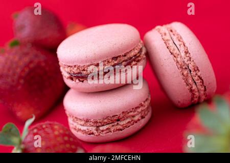 Gros plan studio de paysages de délicieux biscuits de macaron français colorés sur fond rouge avec des fraises. Banque D'Images
