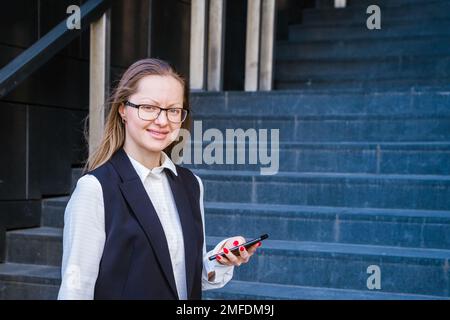 Femme d'affaires réussie parlant sur un téléphone mobile tout en marchant à l'extérieur près du centre d'affaires. Femme d'affaires en costume et lunettes. Banque D'Images