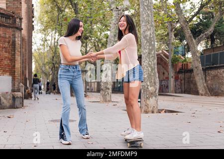 femme enseignant à son ami de monter à bord d'un skateboard Banque D'Images