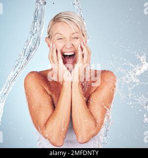 Soin de la peau, excitée et portrait d'une femme avec un jet d'eau isolé sur un fond bleu. Soins de soi, heureux et visage d'un modèle de beauté âgé Banque D'Images