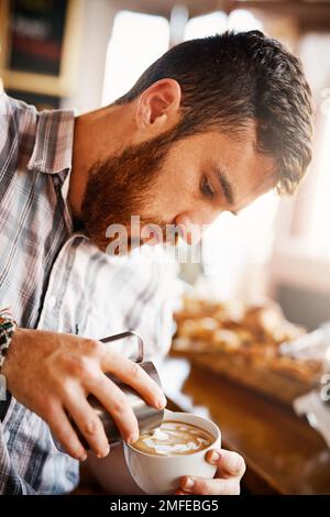 C'est un art à lui seul. Une dose courte d'un barista qui verse de la mousse de lait dans une tasse de café chaud pour en faire une photo. Banque D'Images