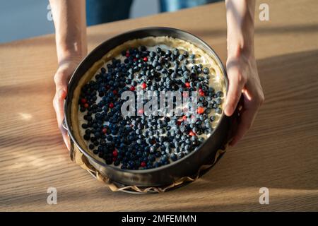 Vue de dessus des mains avec moule rond pour gâteau avec baies fraîches disposées sur la pâte pour table de fête Banque D'Images