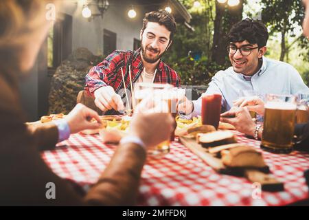 Un groupe d'amis se réunissent autour d'une table à carreaux dans un patio arrière-cour, en riant et en appréciant des bières et des nachos lors d'une journée ensoleillée Banque D'Images