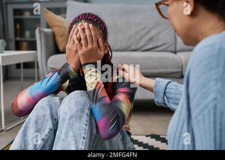 Portrait d'une adolescente pleurs se cachant face avec une mère ou un thérapeute la réconfortant Banque D'Images