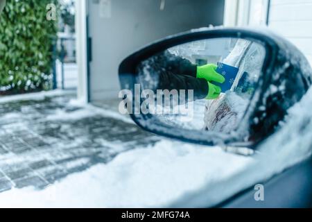 L'adolescent nettoie la voiture après une chute de neige, en enlevant la neige et en raclant la glace Banque D'Images