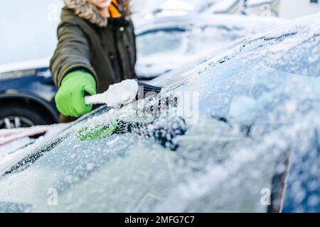 L'adolescent nettoie la voiture après une chute de neige, en enlevant la neige et en raclant la glace Banque D'Images