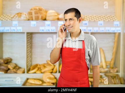 un commerçant avec un tablier utilisant un smartphone à la boulangerie Banque D'Images