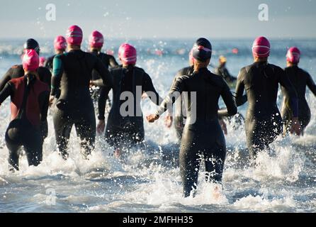 Groupe de participants de triathlon courant dans l'eau pour la partie de natation de la course, des éclaboussures d'eau et des athlètes de course à pied Banque D'Images