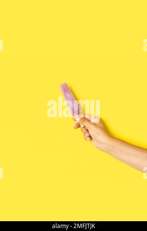 Femme main tenant la popsicle d'eau sur un fond jaune avec espace de copie Banque D'Images