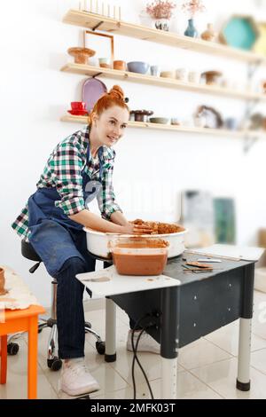 Joyeuse sculptrice pendant qu'elle fait pot d'argile sur la roue de poterie. Idée de petite entreprise et d'entrepreneuriat. Loisirs, loisirs et loisirs à la maison Banque D'Images