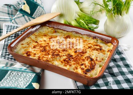 Un gratin de fenouil cuit servi dans une assiette blanche, avec du fenouil frais à proximité Banque D'Images