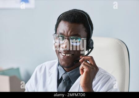 Portrait d'un jeune médecin noir portant un casque et souriant à l'appareil photo au bureau Banque D'Images