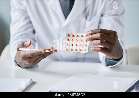 Gros plan d'un médecin afro-américain méconnaissable tenant des comprimés à l'appareil photo et pointant Banque D'Images