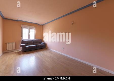 Salle de séjour vide d'une maison peinte dans une couleur pêche unie et un canapé solitaire à côté d'une fenêtre Banque D'Images