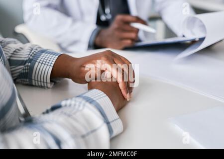 Gros plan de la femme noire à l'écoute du médecin en clinique avec l'accent sur les mains de femme accrochées, l'espace de copie Banque D'Images