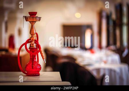 Un gros plan du narguilé rouge avec flacon en verre sur une surface en bois dans un café avec un fond flou Banque D'Images