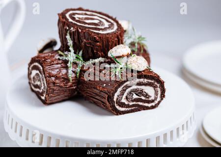 Dessert français appelé Yule log ou bûche de Noël avec champignons merengue et feuilles sur vitrage au chocolat. Placé devant l'arbre de Noël. Déc Banque D'Images