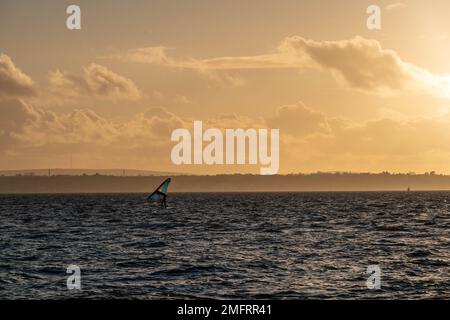 Planche à voile à Hill Head Hampshire Angleterre avec l'île de Wight et une brume orange du soleil se coucher en arrière-plan Banque D'Images