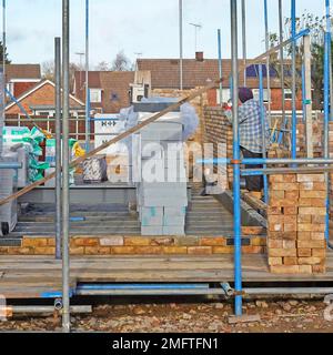 Bricklayer travaillant parmi les matériaux de construction d'échafaudages et de construction les premières étapes de la structure de mur de cavité de brique de la nouvelle maison indépendante Angleterre Royaume-Uni Banque D'Images