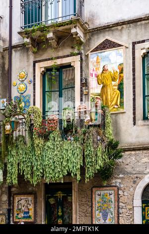 Façade d'une maison avec une porte peinte avec art, balcon, carreaux de céramique et fleurs en pots dans l'une des ruelles de la destination touristique de Taormin Banque D'Images