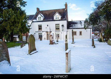 Vue de la neige couverte église paroissiale St Mary à Astbury près de Congleton Cheshire Angleterre de la maison publique Egerton Arms en hiver neige Banque D'Images
