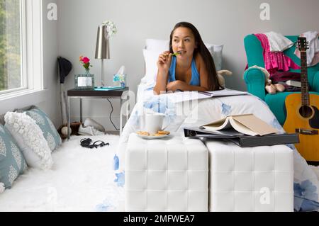 Une adolescente a l'air pensive dans sa chambre comme elle écrit dans un carnet. Banque D'Images