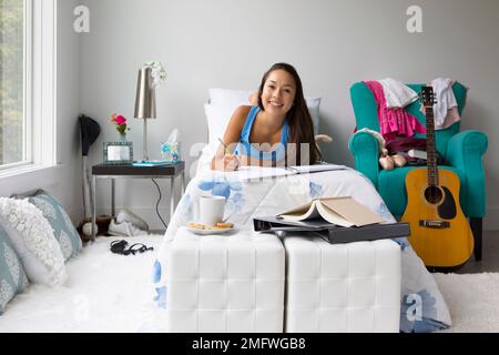 Une adolescente fait ses devoirs sur son lit dans sa chambre. Banque D'Images