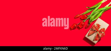 Concept cadeau de la Saint-Valentin. Fond rouge romantique avec bouquet de tulipes lumineux et boîte surprise enveloppée. Lumière dure, ombre foncée, style minimaliste, Banque D'Images