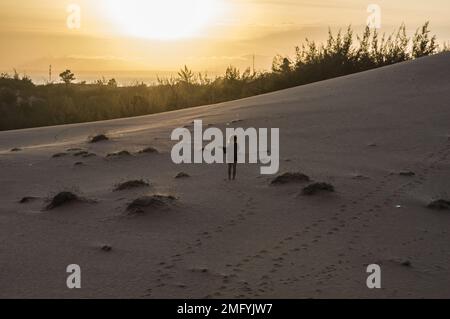 Silhouette d'une femme solitaire, éclairée par le soleil, sur les dunes de sable rouge de Mui ne, province de Phan Thiet, Vietnam, une attraction touristique majeure. Banque D'Images