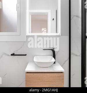 La salle de bains lumineuse présente un style élégant et minimaliste, avec un lavabo blanc brillant placé contre un magnifique miroir encadré de noir, créant un et moderne Banque D'Images