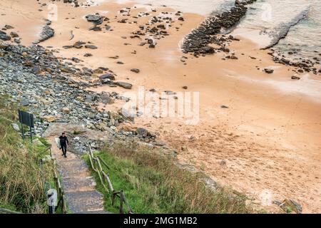 Vue aérienne d'un homme vêtu d'une combinaison noire et d'une planche de surf dans sa main en montant les escaliers sur la plage de Langre, Cantabrie, nord de l'Espagne. Banque D'Images