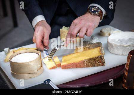 un serveur découpe un fromage pour son client dans un hôtel Banque D'Images