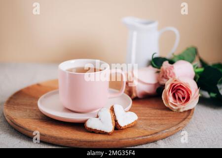 Une tasse de thé, des biscuits en forme de cœur, des roses roses roses et un pot de lait sur un plateau en bois Concept de la Saint-Valentin. Petit-déjeuner le matin. Gros plan. Banque D'Images