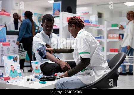 Consultation du pharmacien, mesure de la pression artérielle du patient. Femme examinant l'homme afro-américain santé en pharmacie, diagnostic de maladie cardiovasculaire, examen médical Banque D'Images