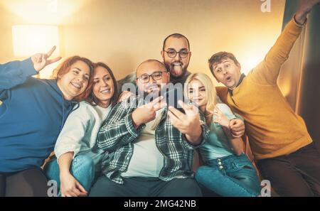 Des amis à la maison font la fête en prenant le selfie, en riant, en ayant du bon temps. Utilisez le téléphone pour passer des appels vidéo à distance et prendre des photos de selfie de diversité. Banque D'Images