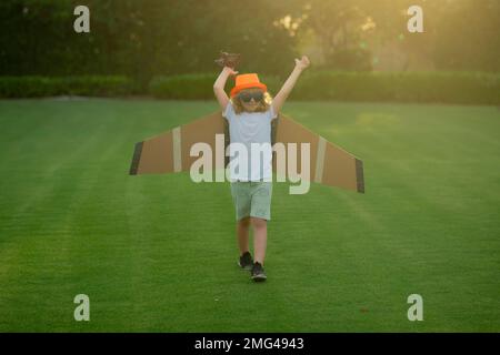 Enfance à la campagne. Joyeux enfant jouant avec des ailes de papier jouet à l'extérieur dans le champ d'été. Concept de voyage et de vacances pour enfants. Imagination et liberté. Banque D'Images