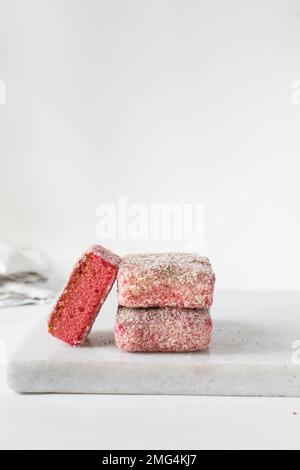 Lamingtons roses sur un plateau en marbre, lamingtons de framboises australiens, gâteau couvert de noix de coco déshydratées Banque D'Images